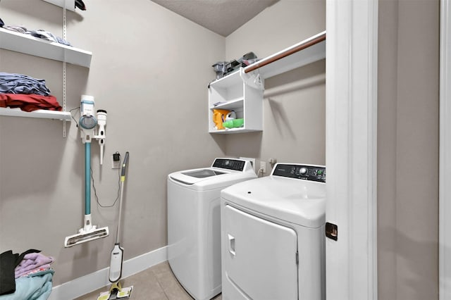 clothes washing area with washing machine and clothes dryer, a textured ceiling, and light tile patterned floors