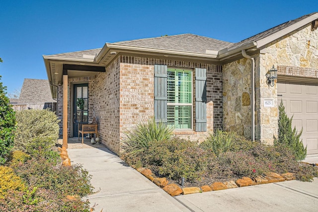 view of exterior entry with a garage, stone siding, brick siding, and a shingled roof