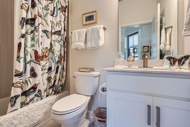 bathroom with a textured wall, toilet, shower / tub combo, vanity, and baseboards