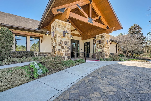 entrance to property with stone siding, roof with shingles, and stucco siding