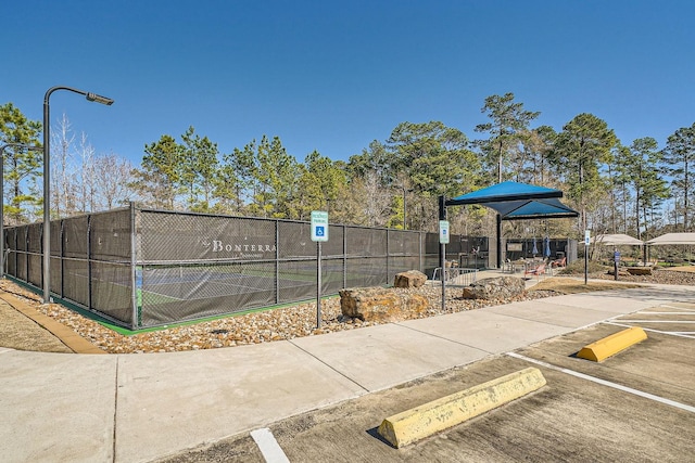 view of property's community featuring a tennis court and fence