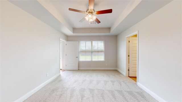 empty room with baseboards, visible vents, a raised ceiling, and light colored carpet