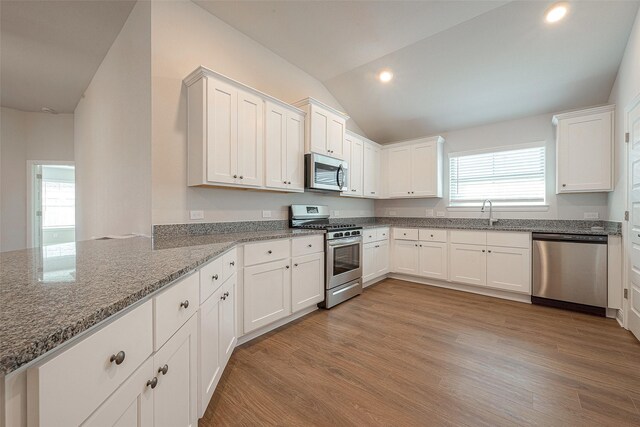 kitchen featuring light stone counters, appliances with stainless steel finishes, vaulted ceiling, and white cabinets