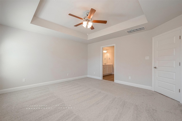 empty room with a raised ceiling, light carpet, and ceiling fan