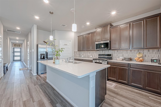 kitchen featuring a kitchen island with sink, sink, stainless steel appliances, and hanging light fixtures