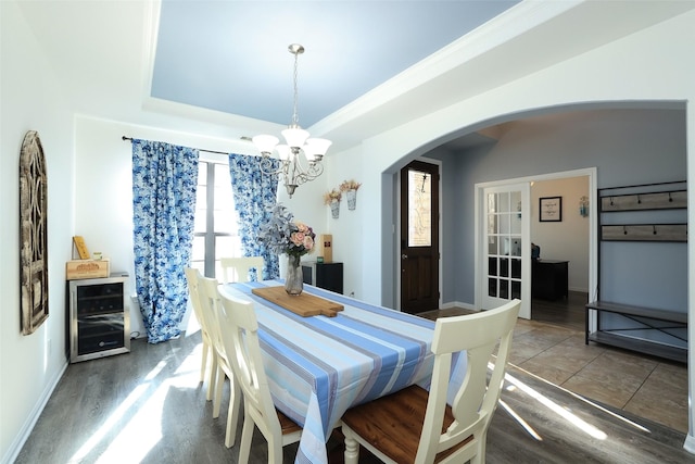 tiled dining space featuring wine cooler, a notable chandelier, and a raised ceiling