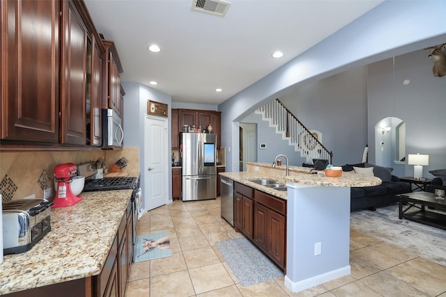 kitchen with sink, appliances with stainless steel finishes, an island with sink, light tile patterned flooring, and decorative backsplash