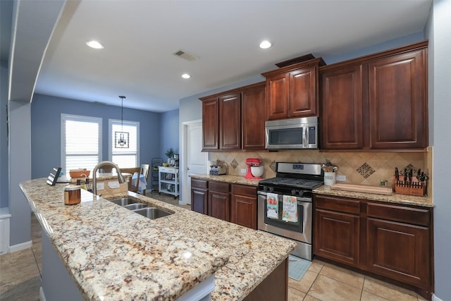 kitchen with stainless steel appliances, sink, a kitchen island with sink, and backsplash