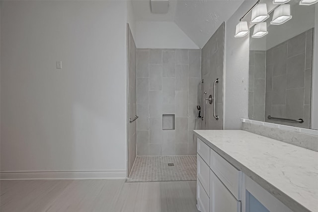 bathroom with a tile shower, vanity, and lofted ceiling