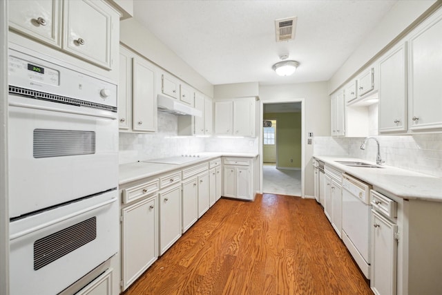 kitchen featuring sink, white cabinets, decorative backsplash, light hardwood / wood-style floors, and white appliances