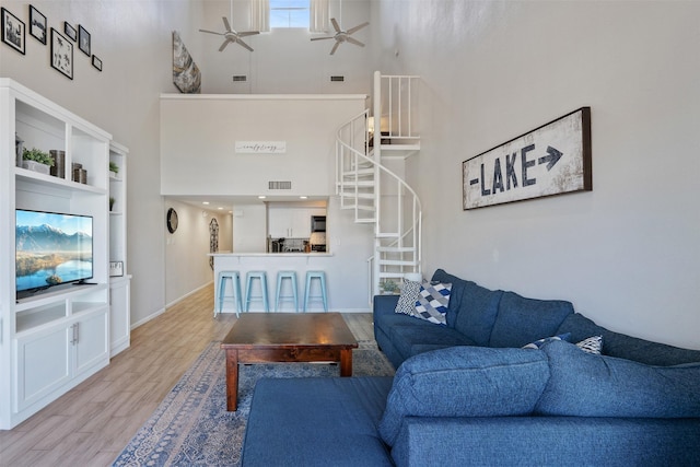 living room with a high ceiling, ceiling fan, and light hardwood / wood-style floors