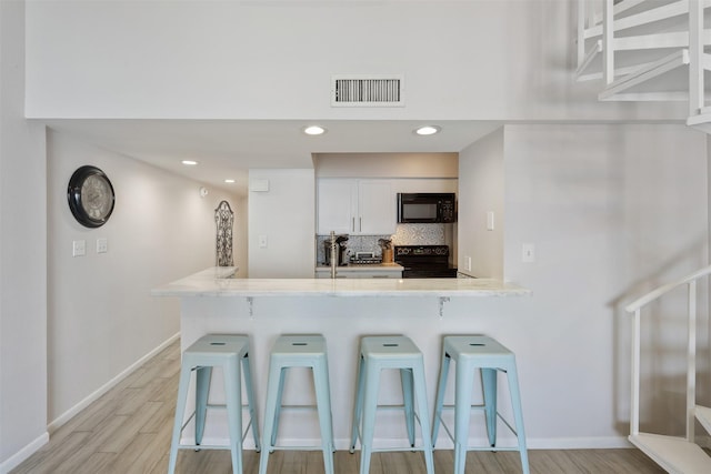 kitchen with a kitchen bar, black appliances, white cabinets, light hardwood / wood-style floors, and backsplash