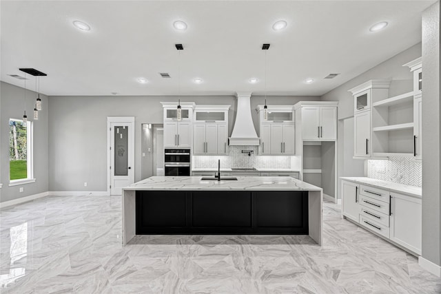 kitchen featuring decorative light fixtures, custom range hood, and a large island with sink