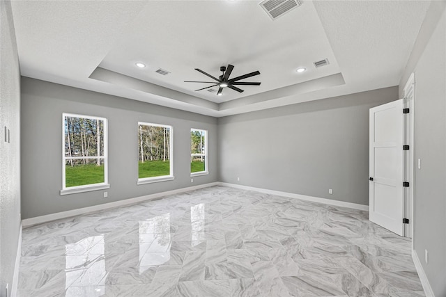 empty room with ceiling fan, a tray ceiling, and a textured ceiling