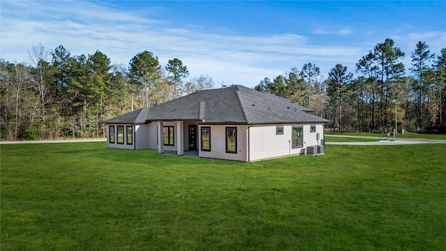 rear view of house with central air condition unit and a lawn