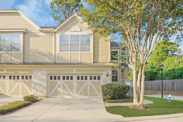 view of front of property with stone siding, fence, concrete driveway, an attached garage, and a shingled roof