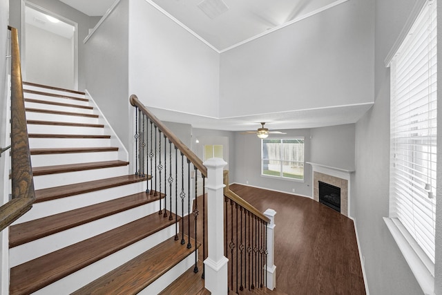 staircase with a tiled fireplace, a high ceiling, wood finished floors, and a ceiling fan