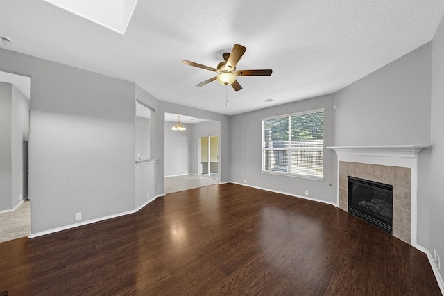 unfurnished living room featuring a tiled fireplace, ceiling fan with notable chandelier, baseboards, and wood finished floors