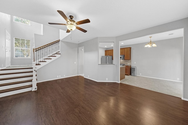 unfurnished living room featuring ceiling fan with notable chandelier, stairs, baseboards, and wood finished floors