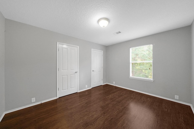 unfurnished bedroom featuring dark wood-style floors, visible vents, a textured ceiling, and baseboards