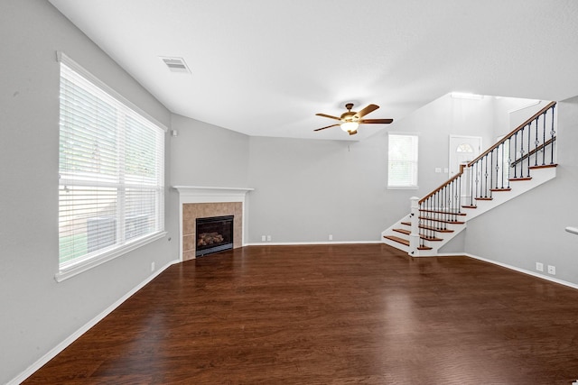 unfurnished living room with visible vents, wood finished floors, stairway, baseboards, and a tile fireplace