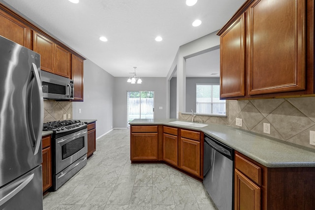 kitchen featuring a sink, stainless steel appliances, an inviting chandelier, a peninsula, and brown cabinetry