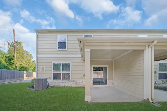 rear view of property with fence, central AC, a yard, a patio area, and stone siding