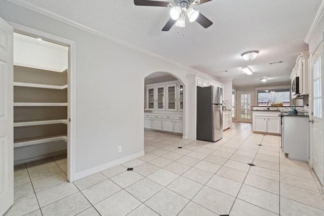 kitchen with light tile patterned flooring, sink, ornamental molding, appliances with stainless steel finishes, and white cabinets