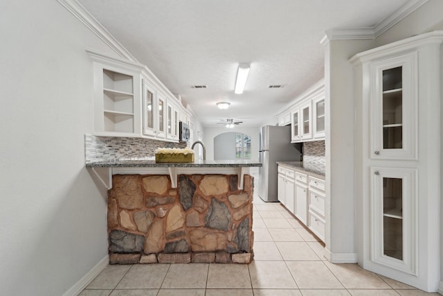 kitchen featuring backsplash, kitchen peninsula, light tile patterned floors, and white cabinets