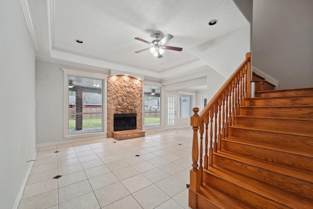 unfurnished living room featuring a stone fireplace, a raised ceiling, ceiling fan, and light tile patterned flooring