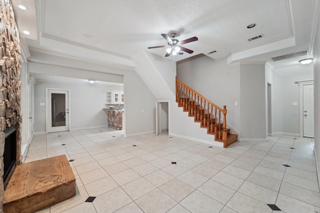 tiled living room featuring ceiling fan, a stone fireplace, and a raised ceiling