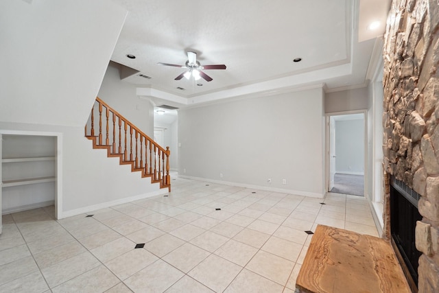 unfurnished living room with a stone fireplace, built in features, light tile patterned floors, ceiling fan, and a raised ceiling