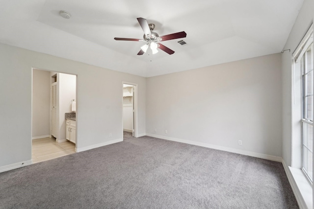 unfurnished bedroom featuring connected bathroom, a spacious closet, ceiling fan, a raised ceiling, and a closet