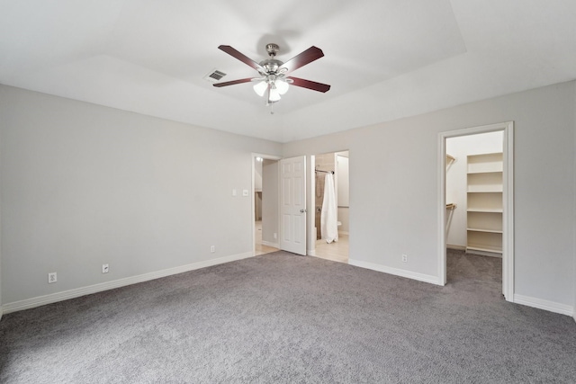 unfurnished bedroom featuring connected bathroom, carpet flooring, a spacious closet, ceiling fan, and a closet