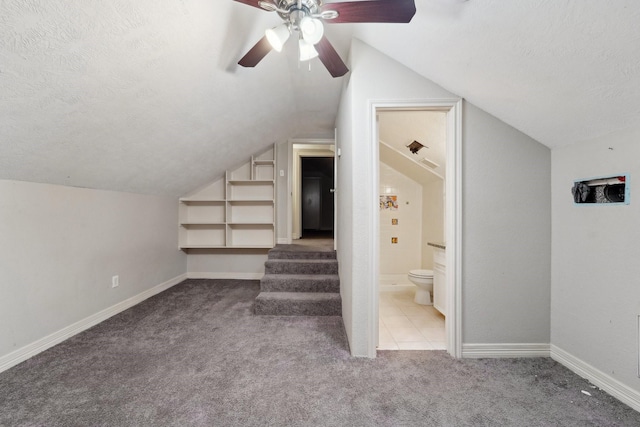 bonus room featuring vaulted ceiling, built in features, light colored carpet, ceiling fan, and a textured ceiling