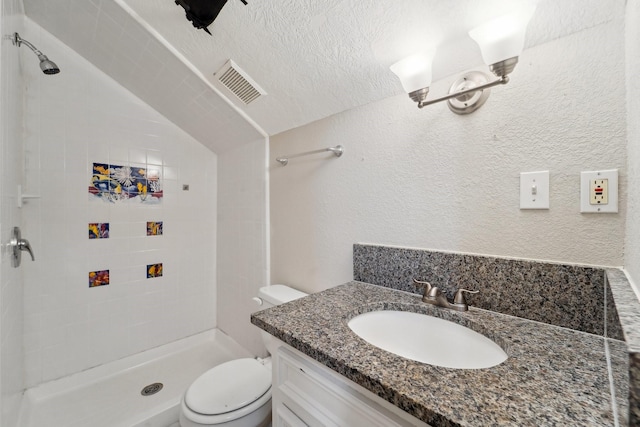 bathroom with vanity, a tile shower, a textured ceiling, and toilet