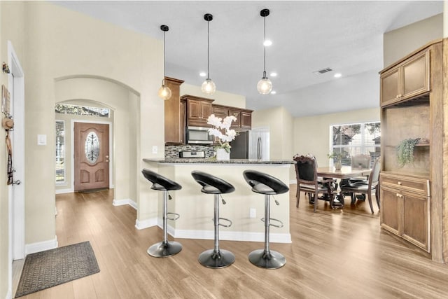 kitchen featuring appliances with stainless steel finishes, dark stone counters, hanging light fixtures, decorative backsplash, and kitchen peninsula