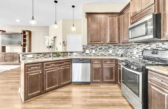 kitchen featuring light stone counters, decorative light fixtures, kitchen peninsula, stainless steel appliances, and decorative backsplash