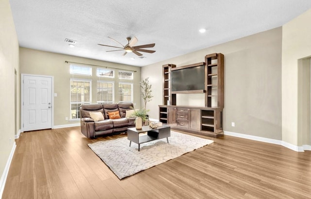 living room featuring hardwood / wood-style flooring, ceiling fan, and a textured ceiling