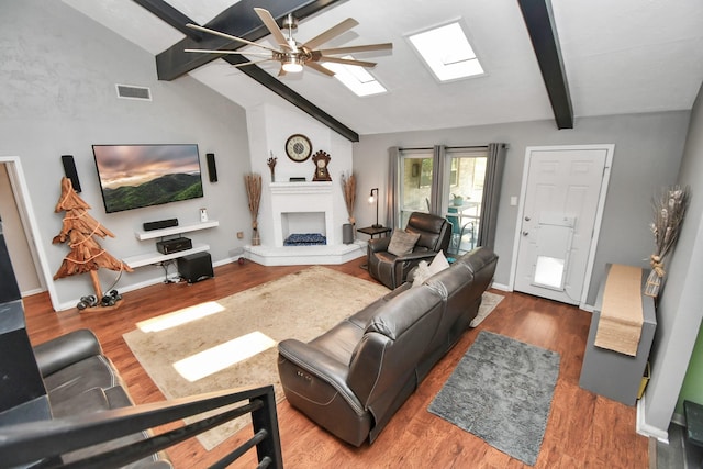 living room featuring hardwood / wood-style floors, vaulted ceiling with skylight, and ceiling fan