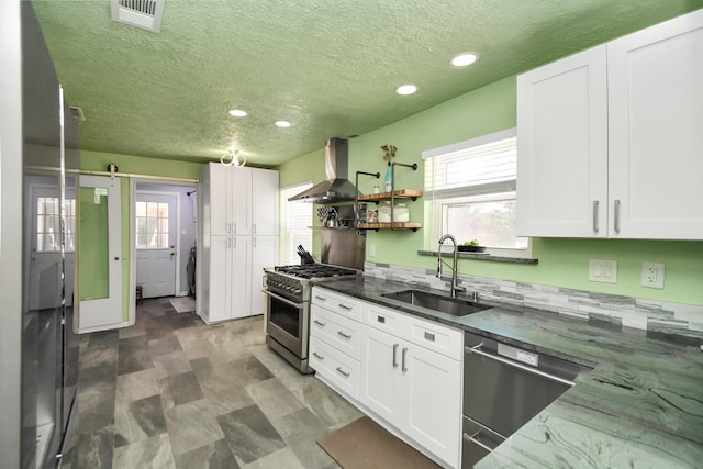 kitchen featuring sink, white cabinetry, appliances with stainless steel finishes, a barn door, and wall chimney range hood