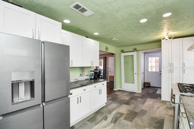 kitchen with tasteful backsplash, a barn door, white cabinets, and appliances with stainless steel finishes