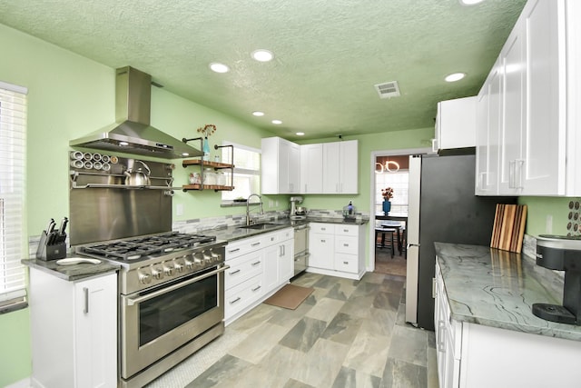 kitchen featuring sink, white cabinetry, dark stone counters, stainless steel appliances, and wall chimney range hood