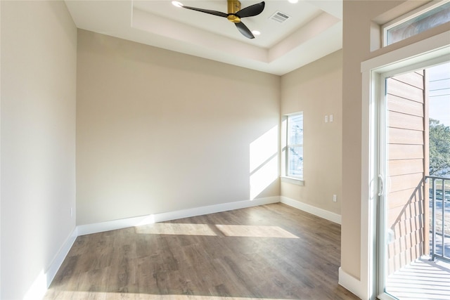 spare room featuring wood finished floors, a raised ceiling, visible vents, and baseboards