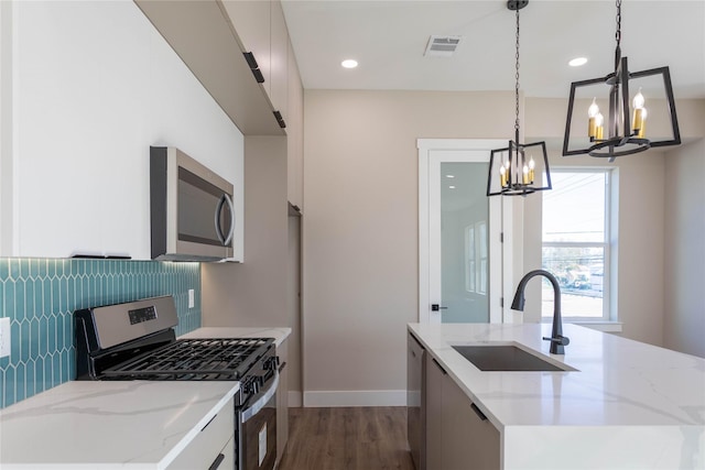 kitchen with a center island with sink, modern cabinets, appliances with stainless steel finishes, decorative light fixtures, and a sink