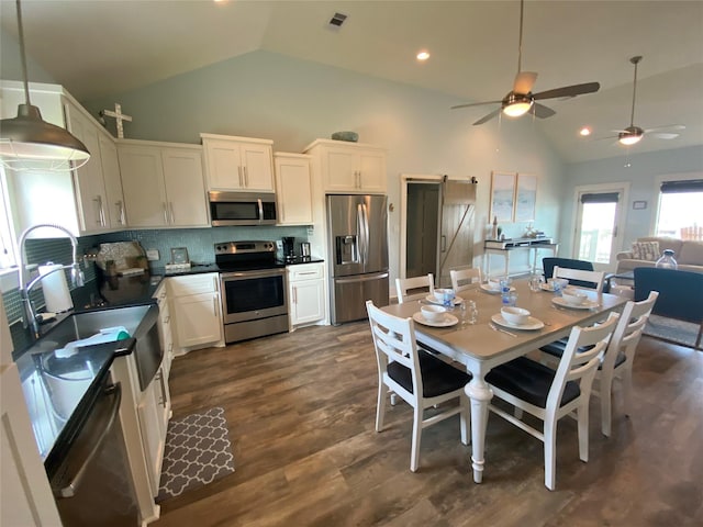 kitchen with sink, backsplash, stainless steel appliances, white cabinets, and a barn door