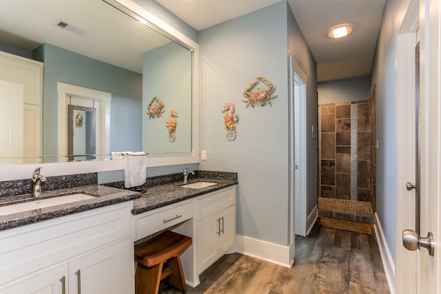 bathroom featuring wood-type flooring, a tile shower, and vanity