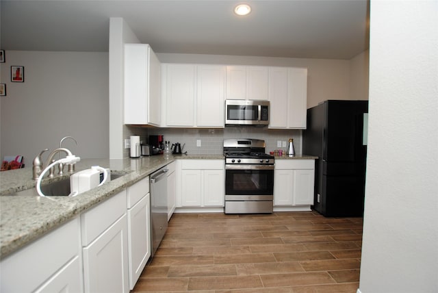 kitchen featuring white cabinetry, sink, backsplash, stainless steel appliances, and light stone countertops