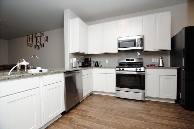 kitchen featuring appliances with stainless steel finishes, light stone countertops, decorative backsplash, and white cabinets