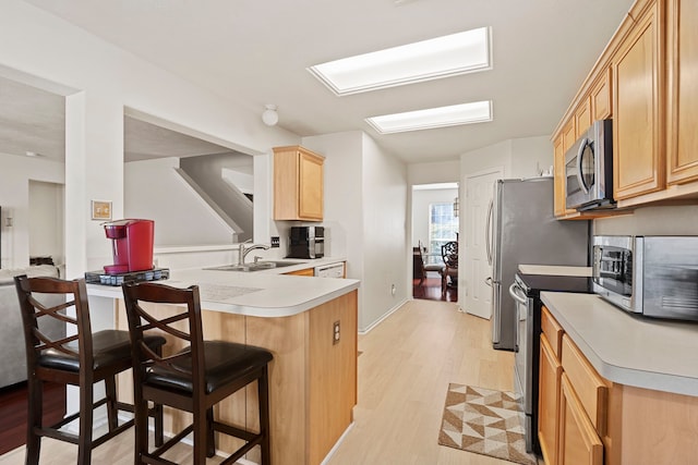 kitchen featuring appliances with stainless steel finishes, sink, a breakfast bar area, kitchen peninsula, and light hardwood / wood-style flooring